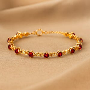 Peut inclure: Un bracelet doré composé d'une série de pierres précieuses rondes rouge foncé serties dans des maillons métalliques. Le design alterne entre les pierres rouges circulaires et de petits connecteurs métalliques en forme d'infini.