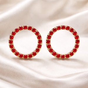 Peut inclure: Une paire de boucles d'oreilles circulaires dotées d'une monture en métal doré sertie d'une rangée continue de petites pierres rondes à facettes d'un rouge éclatant. Le design se compose de deux anneaux ouverts identiques ornés de gemmes rouges.