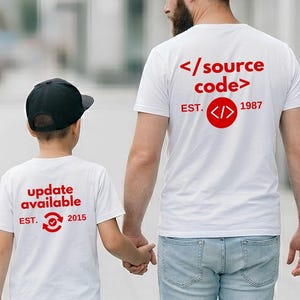 Könnte beinhalten: Zwei weiße T-Shirts mit rotem Text und Grafiken. Das größere T-Shirt zeigt den Text </source code> und EST. 1987 mit einem Code-Symbol. Das kleinere T-Shirt zeigt den Text update available und EST. 2015 mit einem kreisförmigen Aktualisierungssymbol.