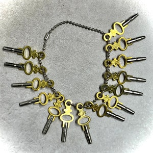 Puede incluir: Un juego de 12 llaves de reloj en una cadena plateada. Las llaves son de latón y tienen diferentes tamaños de cabeza. Las llaves se utilizan para dar cuerda y ajustar los relojes.