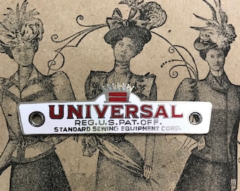 May include: A white metal sewing machine badge with red lettering that reads "UNIVERSAL REG. U.S. PAT. OFF. STANDARD SEWING EQUIPMENT CORP."