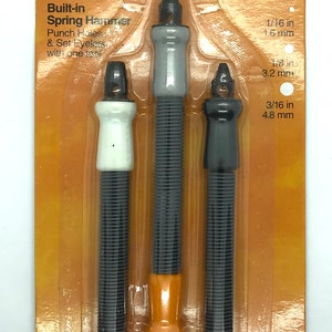 May include: A set of three Fiskars eyelet setters with a built-in spring hammer. The tools are orange and gray with black tips. The set includes three sizes: 1/16 in (1.6 mm), 1/8 in (3.2 mm), and 3/16 in (4.8 mm). The packaging is orange and features the Fiskars logo and the text "Lifetime Warranty".