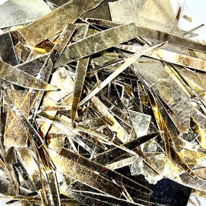 Può includere: Un mucchio di sottili scaglie di mica dorate e marroni iridescenti. Le scaglie hanno una forma irregolare e un bagliore metallico scintillante.