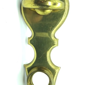 Könnte beinhalten: Ein goldfarbener Türknauf aus Metall mit einem dekorativen Design. Der Knauf hat einen Ring zum Ziehen und ein rundes Loch in der Mitte.