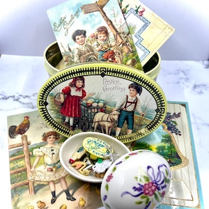 Assortimento di oggetti da collezione pasquali, scatola di latta pasquale vintage, scatola portaoggetti in porcellana Lenox a forma di uovo, cartoline pasquali vittoriane, più ciondoli Cracker Jack