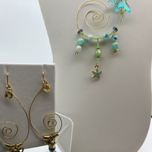 May include: A pair of gold wire earrings with a green stone dangle and a gold wire ear cuff with a spiral design, green and blue beads, and a starfish charm.