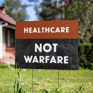 May include: A yard sign with the words "HEALTHCARE" in white block letters above "NOT WARFARE" in white block letters. The top section is orange, and the bottom section is black with a cloud-like design.