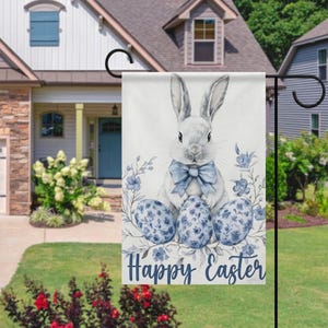 Peut inclure: Drapeau de jardin décoratif de Pâques avec une illustration à l'aquarelle d'un lapin avec un nœud papillon bleu, trois œufs à motifs et des accents floraux. Le drapeau porte l'inscription "Happy Easter" en script bleu.