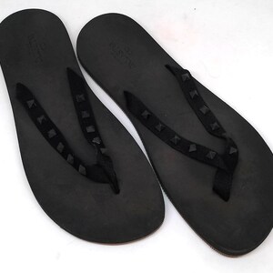 May include: A pair of black leather flip flops with a studded strap. The strap has the word "VALENTINO" printed on it.