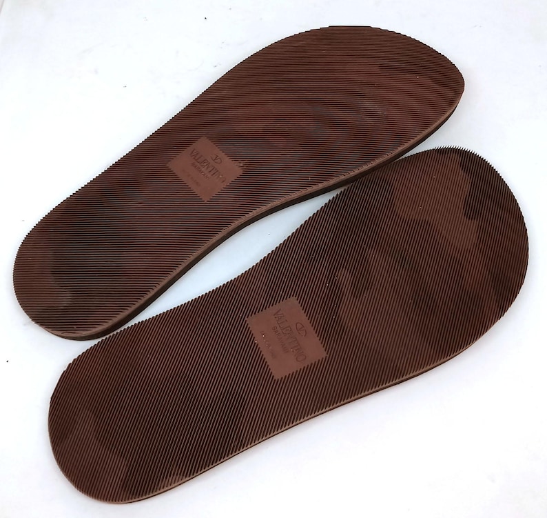 May include: A pair of brown rubber flip-flop soles with the text "VALENTINO GARAVANI" printed on one sole and "32 VALENTINO" printed on the other sole.