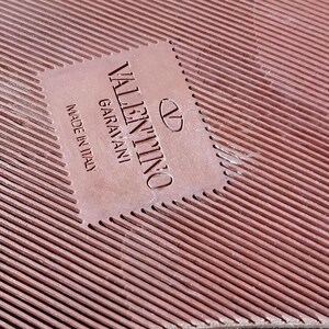 May include: Close-up of a brown leather label with the text "VALENTINO GARAVANI" and "MADE IN ITALY" in white lettering.