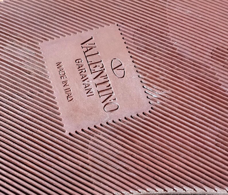 May include: Close-up of a brown leather label with the text "VALENTINO GARAVANI" and "MADE IN ITALY" in white lettering.
