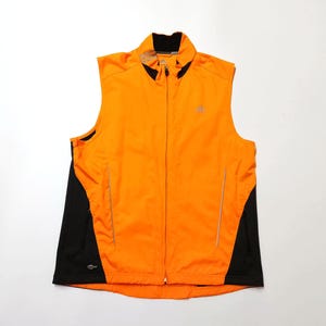 Puede incluir: Chaleco sin mangas Adidas naranja y negro con cremallera completa. El chaleco tiene cuello negro y paneles laterales negros. El logotipo de Adidas es visible en el pecho. El chaleco está hecho de un material ligero, posiblemente resistente al agua.