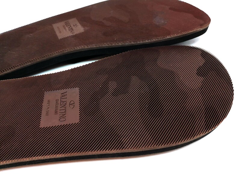 May include: Close-up of the brown rubber soles of a pair of sandals. The soles have a textured pattern and the text "VALENTINO GARAVANI MADE IN ITALY" is printed on the bottom sole.