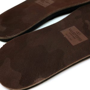 May include: Close-up of the brown rubber soles of a pair of sandals. The sole of one sandal has the text "VALENTINO GARAVANI" and "MADE IN ITALY" printed on it.
