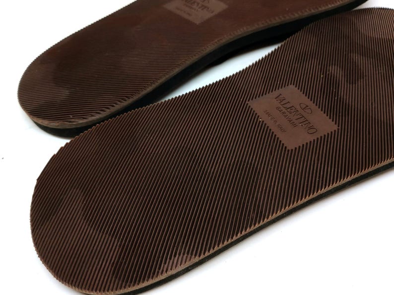 May include: Close-up of the brown rubber soles of a pair of sandals. The sole of one sandal has the text "VALENTINO GARAVANI" and "MADE IN ITALY" printed on it.
