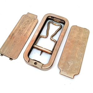 May include: Three antique gold-toned metal pieces with a geometric pattern. The center piece is a rectangular frame with a metal loop inside. The two side pieces are rectangular with a geometric pattern.