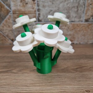 May include: A bouquet of white flower-shaped objects with green stems and centers. The flowers have a layered design, with a rounded center and petal-like edges. The stems are grouped together in a green base.