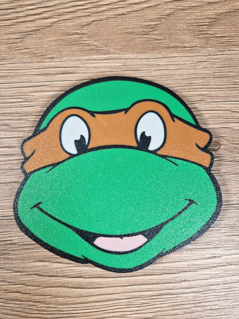 Puede incluir: Una cara de dibujos animados verde y marr&oacute;n con una boca sonriente, ojos blancos y una m&aacute;scara marr&oacute;n. La cara tiene un contorno negro y probablemente sea un personaje de una serie animada popular.