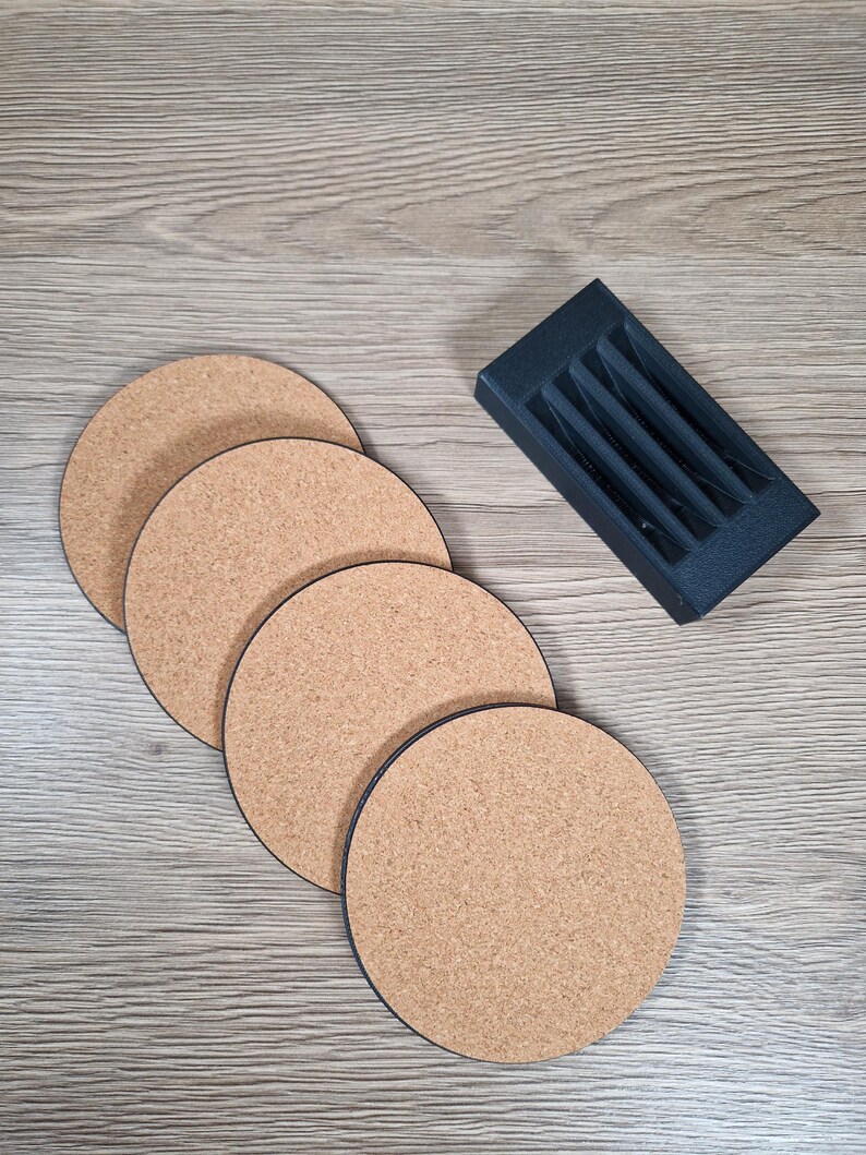 May include: Four round cork coasters with black edges are arranged on a wooden surface. A black holder with slots for pens or pencils sits to the side. The coasters are approximately 4 inches in diameter.