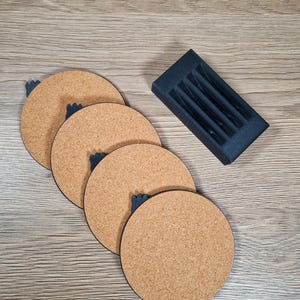 May include: Four round cork coasters with dark blue accents and a matching holder. The coasters are arranged in a diagonal line, showcasing their natural cork texture. The holder is rectangular with slots for coaster storage.