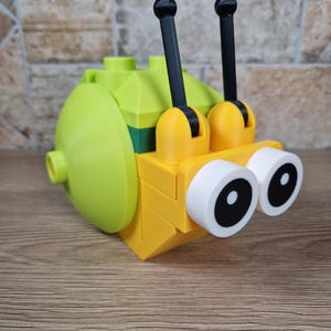 Puede incluir: Un caracol de juguete ensamblado, hecho con bloques de colores. El caracol tiene un cuerpo amarillo brillante, una concha verde lima y antenas negras. Los ojos son blancos con pupilas negras. Este juguete est&aacute; dise&ntilde;ado para el juego creativo.