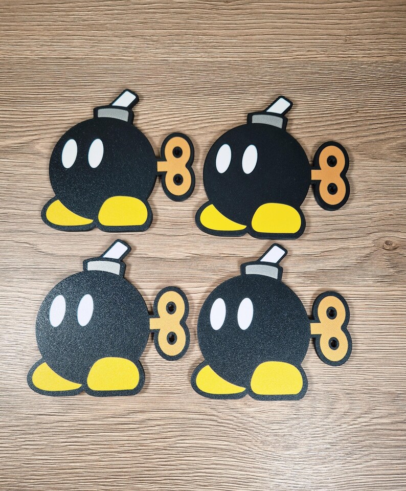 May include: Four black cartoon bomb figures with white oval eyes, yellow feet, and a gray fuse. Each bomb has a brown, figure-eight-shaped winder on its side. The bombs are arranged on a light brown wooden surface.