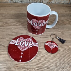 May include: A red mug, coaster, and keychain set with a "Love" design. The design features a heart with a leopard print pattern and white text. The keychain has a gray tassel.