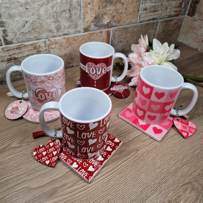 May include: Four white ceramic mugs with various red and pink "Love" designs, each paired with a matching coaster and heart-shaped charm. The mugs feature patterns of hearts and the word "Love".
