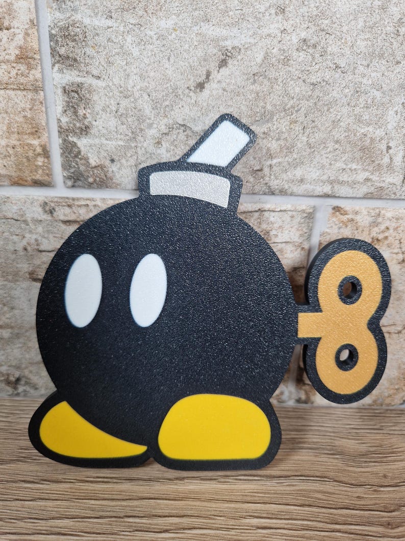 May include: A black cartoon bomb with white eyes, yellow feet, and a silver and white fuse. The bomb has a gold wind-up key on its side. The design is reminiscent of a video game character.