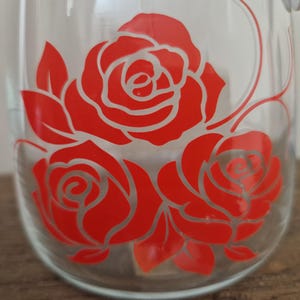 May include: A clear glass jar with a red rose design. The roses are outlined in white and have a vintage look.