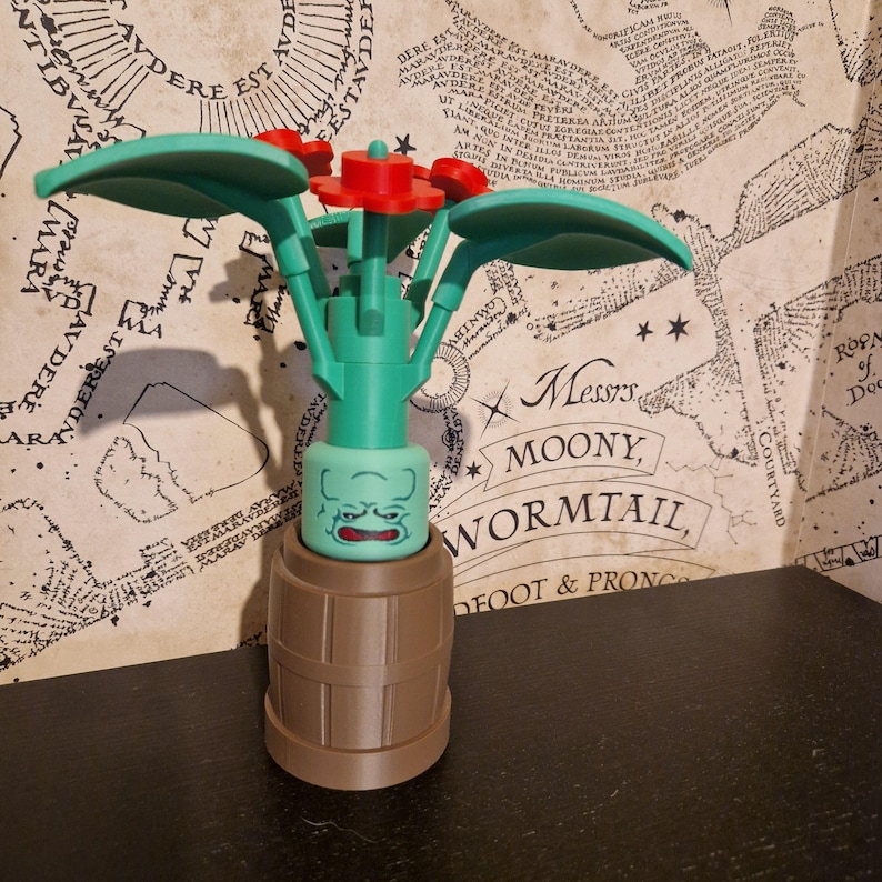 May include: A Lego-style plant with green leaves and red flowers, set in a brown barrel-shaped pot. The plant has a green face with a grumpy expression. The background features a map and text that reads "Messrs. Moony, Wormtail, Foot & Prong."
