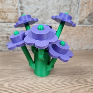 May include: A 3D-printed floral arrangement featuring five stylized flowers. Each flower has a purple, scalloped petal design with a green center. The stems and base are green, creating a vibrant contrast. The arrangement is set against a neutral background.