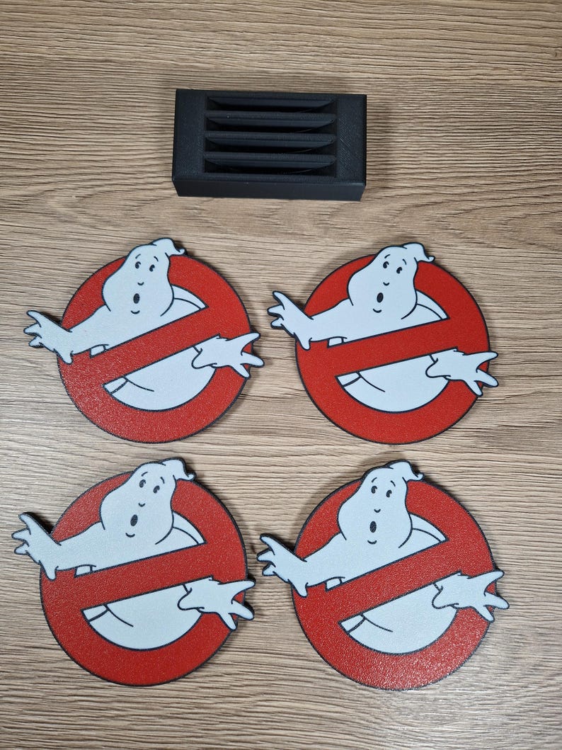 K&ouml;nnte beinhalten: Vier runde Untersetzer mit dem Ghostbusters-Logo: ein wei&szlig;er Geist in einem roten Kreis mit einer diagonalen Linie. Ein schwarzer, rechteckiger Untersetzerhalter ist ebenfalls vorhanden. Die Untersetzer sind aus einem holz&auml;hnlichen Material.