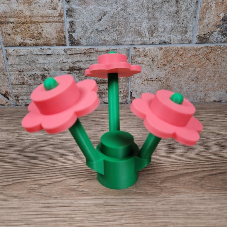 May include: A green and pink decorative flower arrangement. The arrangement features three pink flowers with green centers and a green base. The flowers are arranged on green stems.