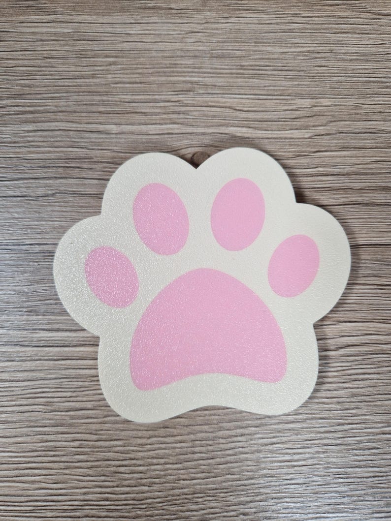 Op de afbeelding: Een pootvormig decoratief item met een witte achtergrond en roze voetzolen. De pootafdruk heeft een glittertextuur. Het item is waarschijnlijk gemaakt van hout of een vergelijkbaar materiaal. Het ontwerp is eenvoudig en schattig, geschikt voor dierenliefhebbers.