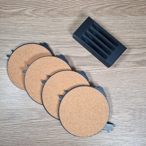 K&ouml;nnte beinhalten: Ein Set aus vier runden Untersetzern aus Kork mit dunkelblauem Rand und einem passenden Halter. Die Untersetzer haben eine nat&uuml;rliche Korkfarbe. Der Halter hat eine rechteckige Form mit Schlitzen f&uuml;r die Untersetzer.
