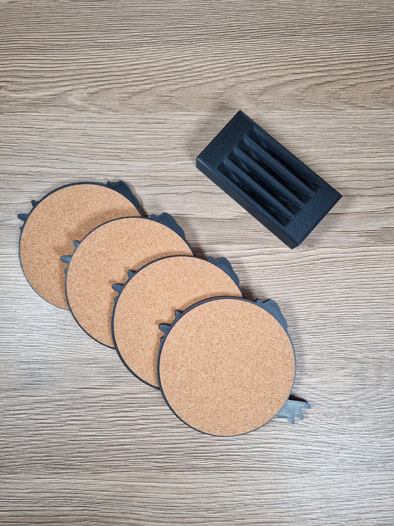 K&ouml;nnte beinhalten: Ein Set aus vier runden Untersetzern aus Kork mit dunkelblauem Rand und einem passenden Halter. Die Untersetzer haben eine nat&uuml;rliche Korkfarbe. Der Halter hat eine rechteckige Form mit Schlitzen f&uuml;r die Untersetzer.