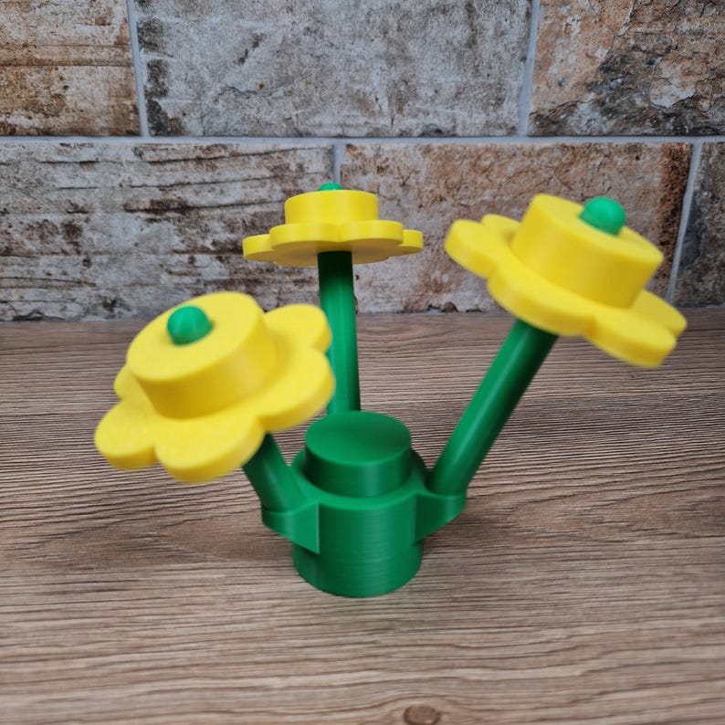 May include: A 3D-printed green and yellow flower sculpture. The sculpture features three flowers with yellow petals and green stems. Each flower has a yellow center with a small green dot. The base is green and has a watering can shape.