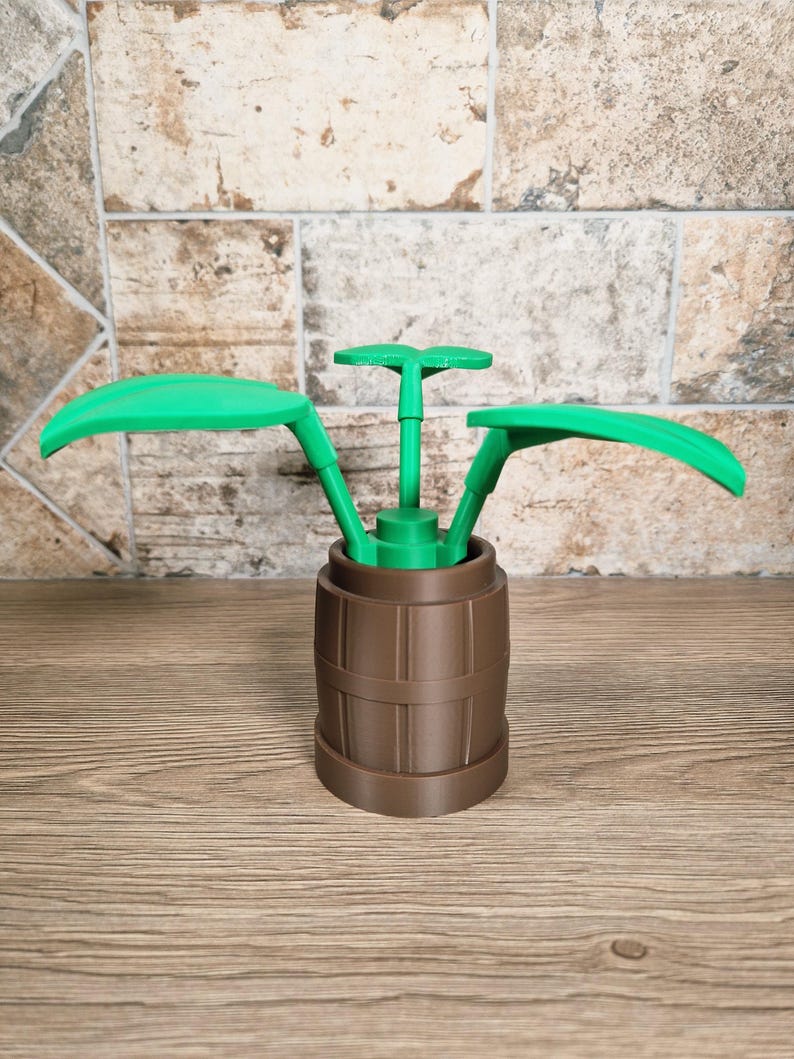 May include: A brown barrel-shaped container with green plant-like elements. The container has a ribbed design, and the green elements include two large, curved leaves and a central stem with a small, flat top. The object is on a wooden surface.