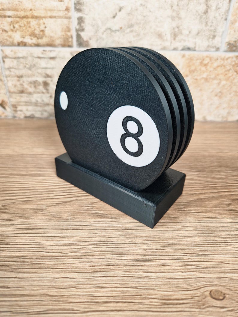 May include: A black wooden coaster set shaped like an eight ball, with a white number eight and a white dot. The coasters are stacked on a black rectangular base, perfect for a game room or bar.