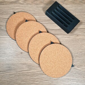 May include: Four round cork coasters with black trim and a black holder. The coasters are a light brown color and are arranged in a row. The holder is black and has four slots to hold the coasters.