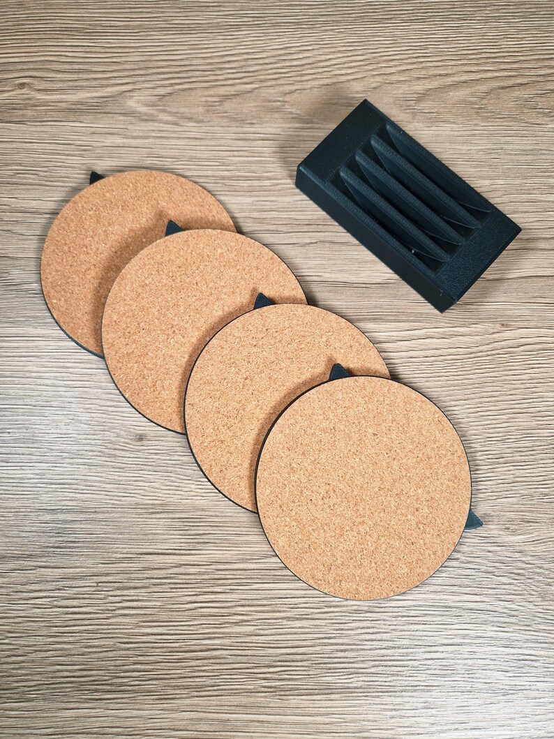 May include: Four round cork coasters with black trim and a black holder. The coasters are a light brown color and are arranged in a row. The holder is black and has four slots to hold the coasters.