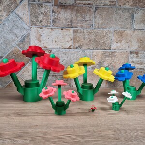 May include: A collection of colorful, stylized flower sculptures. The flowers are red, yellow, blue, pink, and white, with green stems and bases. The flowers are made of plastic and are arranged on a wooden surface.