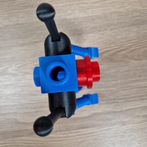 May include: A 3D-printed object featuring a blue cube with a central hole, connected to black arms with rounded ends. A red cylindrical piece is attached to the cube. Blue flexible tubes extend from the cube.
