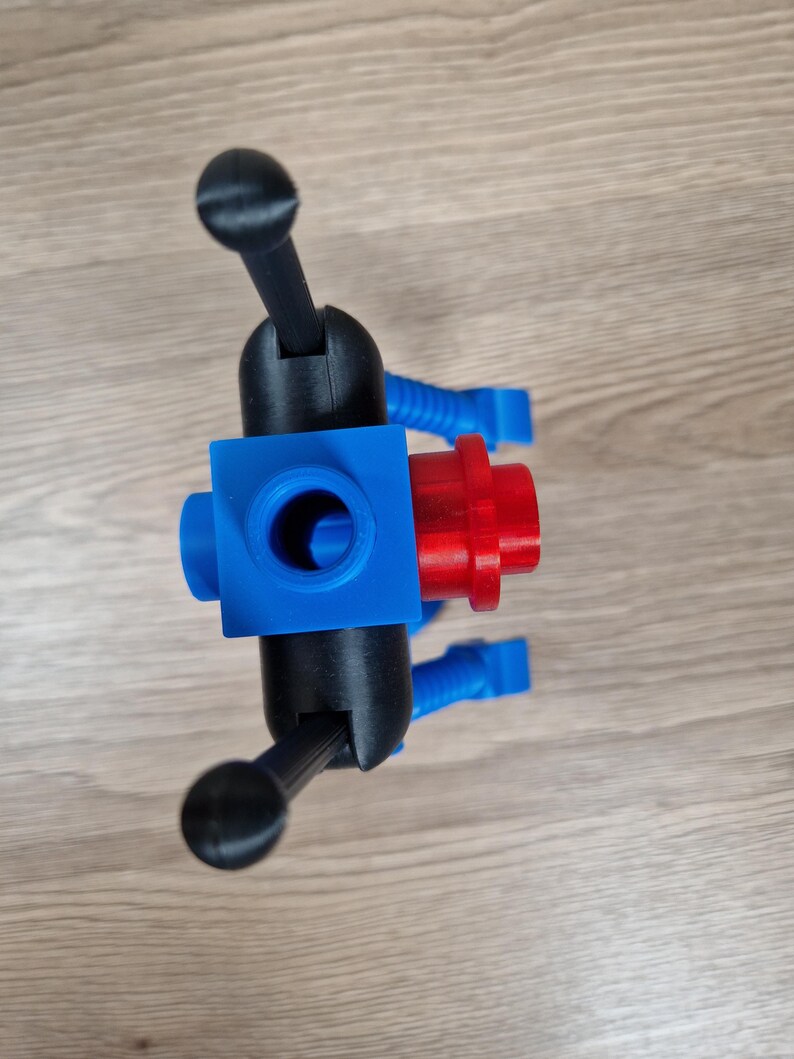 May include: A 3D-printed object featuring a blue cube with a central hole, connected to black arms with rounded ends. A red cylindrical piece is attached to the cube. Blue flexible tubes extend from the cube.