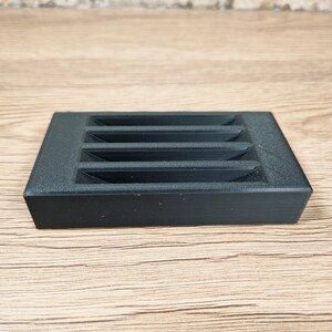Puede incluir: Un objeto rectangular negro con cinco ranuras horizontales. El objeto tiene una superficie texturizada y probablemente est&aacute; hecho de pl&aacute;stico o un material similar. El dise&ntilde;o es simple y funcional.