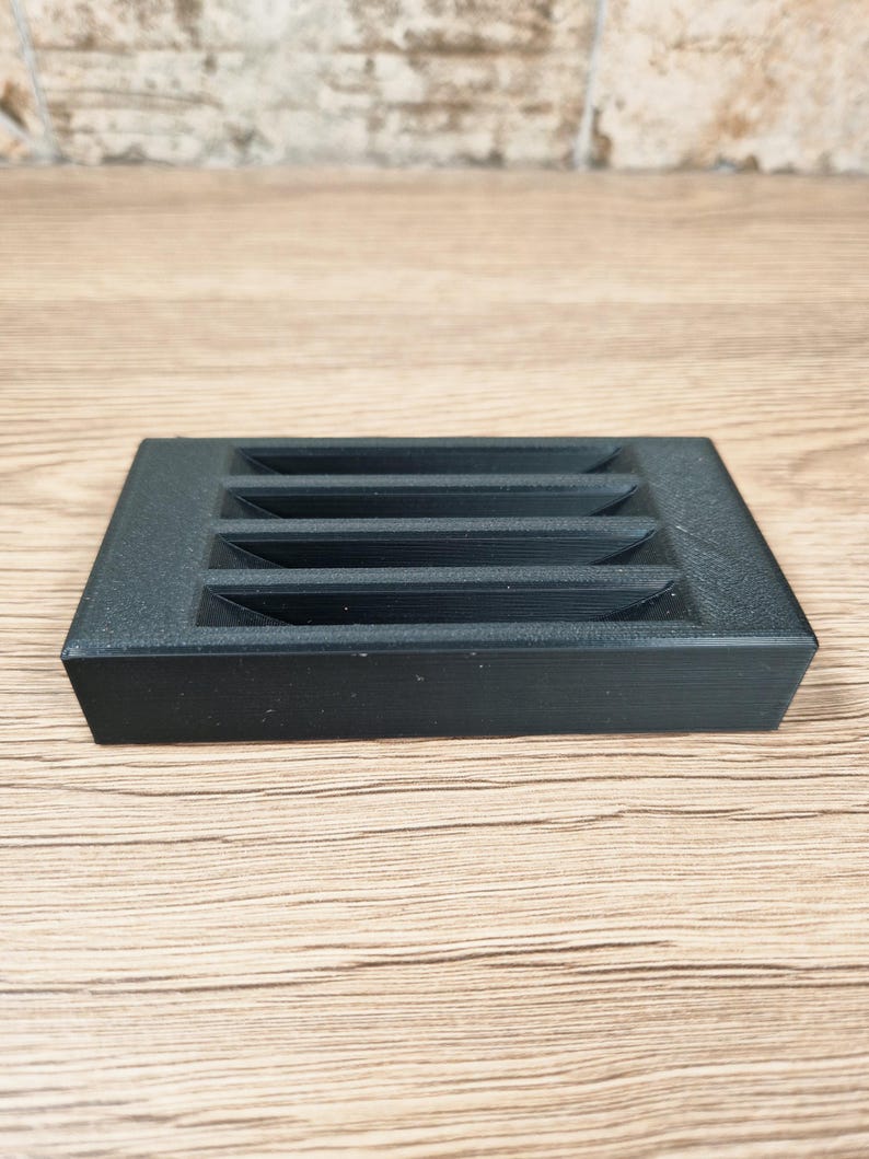 Puede incluir: Un objeto rectangular negro con cinco ranuras horizontales. El objeto tiene una superficie texturizada y probablemente est&aacute; hecho de pl&aacute;stico o un material similar. El dise&ntilde;o es simple y funcional.