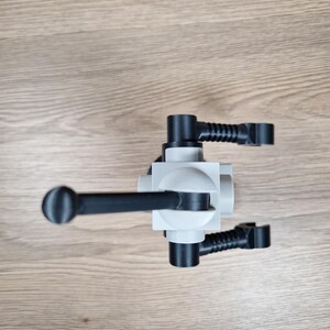 May include: A light gray and black plastic object with a cylindrical handle and multiple black arms extending from a central block. The object is positioned on a light brown wooden surface.