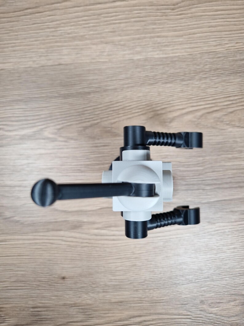 May include: A light gray and black plastic object with a cylindrical handle and multiple black arms extending from a central block. The object is positioned on a light brown wooden surface.